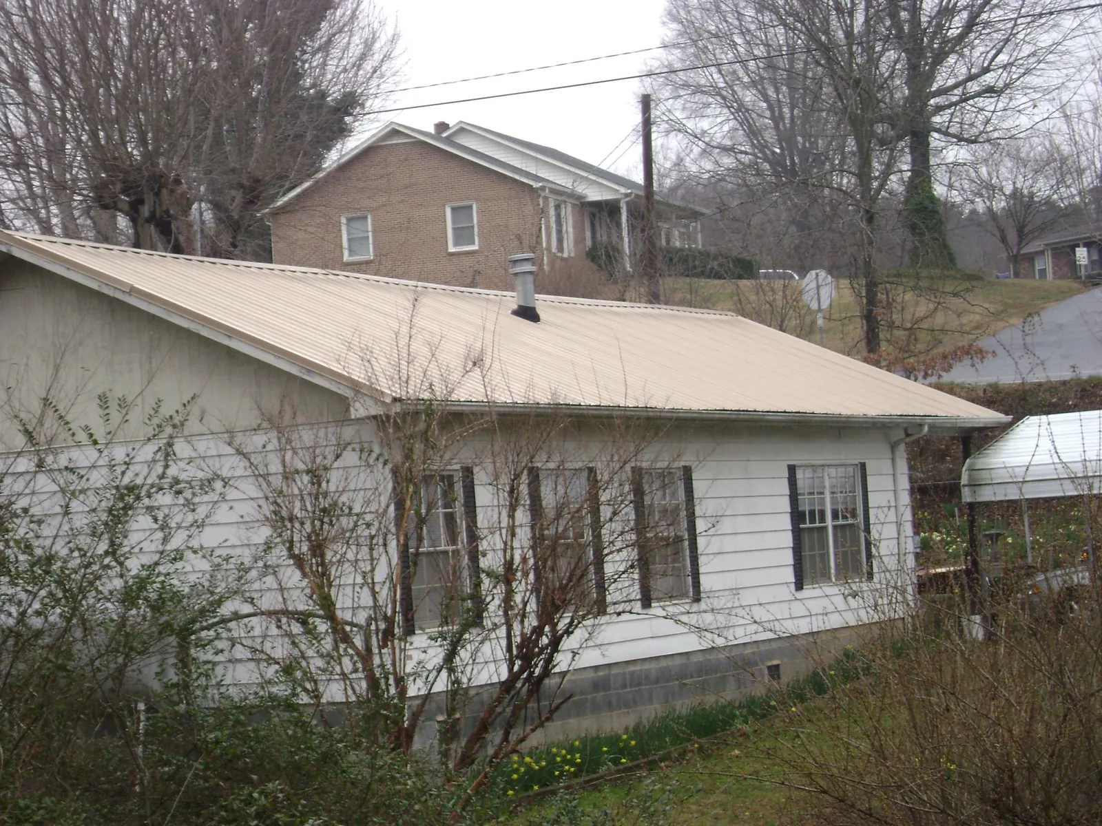 Tan metal roof on a white sided house set into a hillside — Commercial Roofing by Roofing Brothers in Fort Belvoir